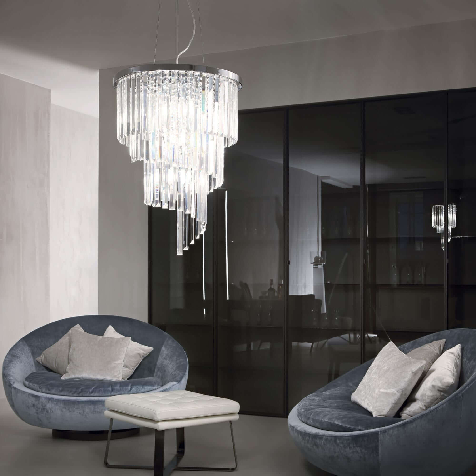 Luxurious Ideal Lux Carlton chandelier with sparkling crystals, hanging in a modern living room with grey sofas.