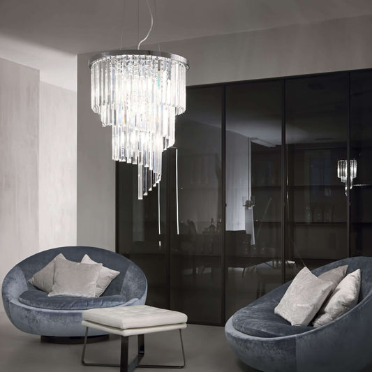 Luxurious Ideal Lux Carlton chandelier with sparkling crystals, hanging in a modern living room with grey sofas.
