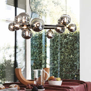 Modern dining room with Ideal Lux Pendelleuchte PERLAGE chandelier featuring 14 glass globes and metallic finish, hanging over a table.
