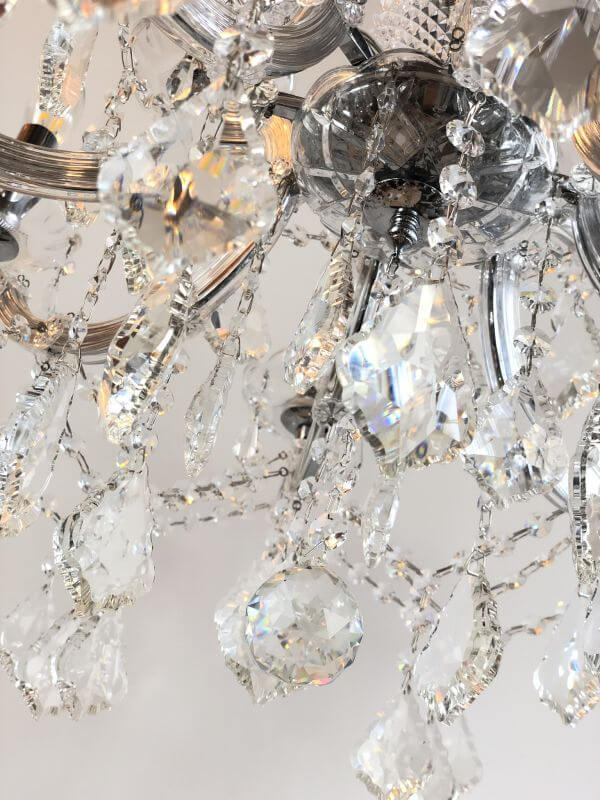 Close-up of a silver 12-light crystal chandelier with glass-covered arms, featuring intricate crystal detailing for elegant lighting.