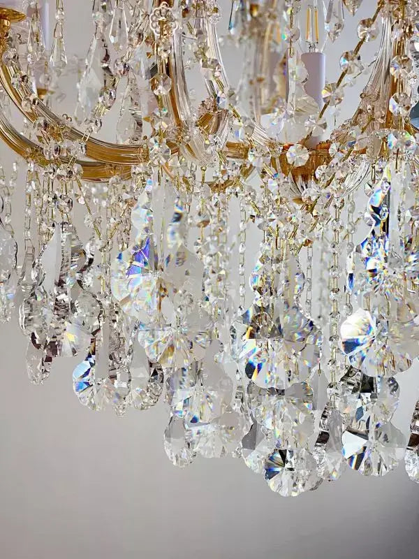 Detail of luxurious crystal chandelier with gold accents and intricate crystal glass arms, featuring sparkling prisms and elegant design.