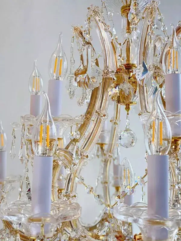 Close-up of gold and crystal chandelier with LED bulbs, featuring ornate decorative elements and crystal arms, Maria Theresia style.