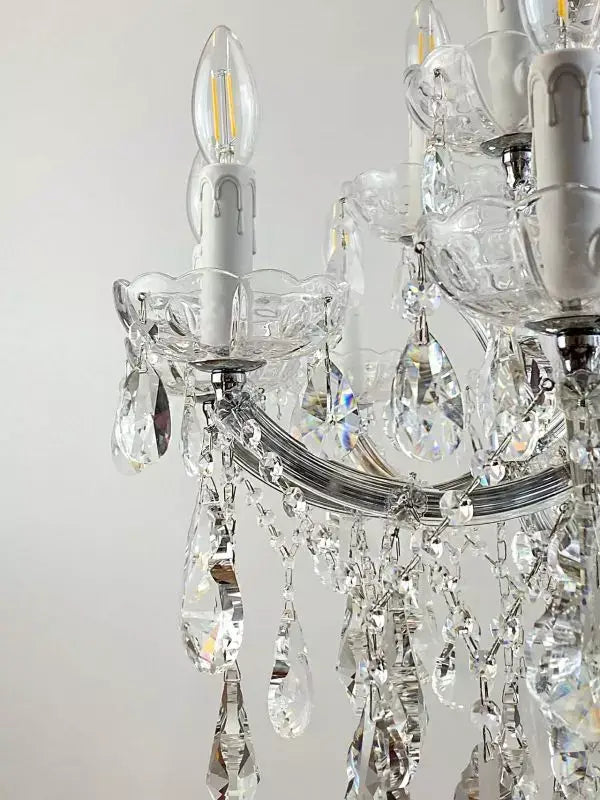 Close-up of a crystal chandelier arm with LED bulbs and hanging cut glass crystals, elegant silver finish, part of a luxury lighting fixture.