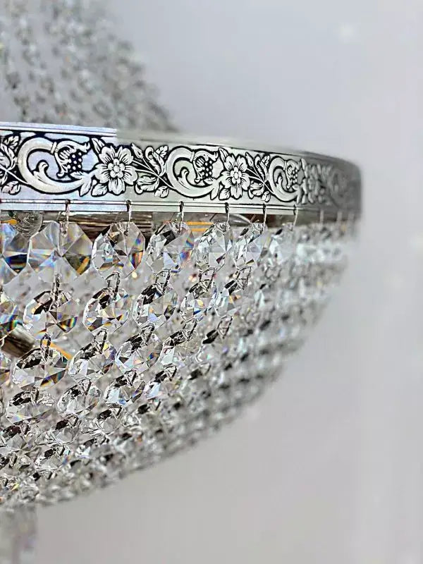 Close-up of Kristall Korblüster PLAZA Ø60cm in silver with cut crystals, featuring intricate floral design on the metal rim.