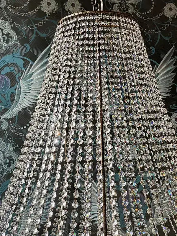 Kristall Korblüster Florence Antik Ø100cm mit funkelnden Kristallen, hängend vor dekorativer Wand, verleiht jedem Raum Eleganz.