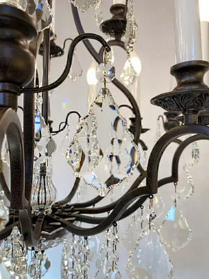 Detail of antique iron crystal chandelier with sparkling crystals, 12 lights, dimmable, hanging elegantly in a Parisian style.