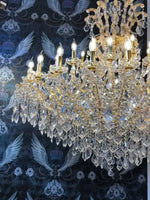 Gold Maria Theresia chandelier with crystal arms and 42 lights, shown in lavish setting, highlighting intricate design and brilliance.