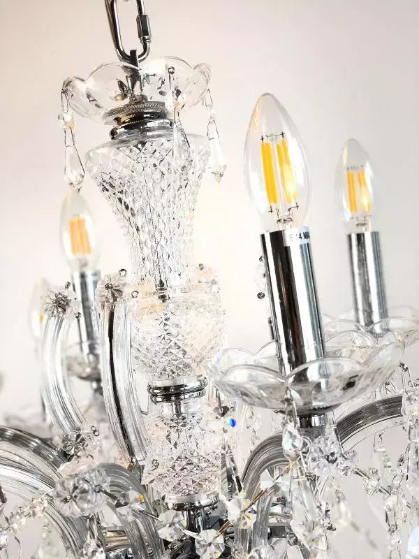 Close-up of a silver crystal chandelier with glass arms and LED bulbs, featuring intricate crystal detailing and chrome finish.