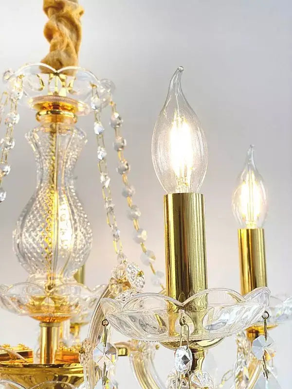 Gold crystal chandelier with intricate design, showcasing sparkling cut lead crystals and three lit candle-style bulbs, elegant decoration.