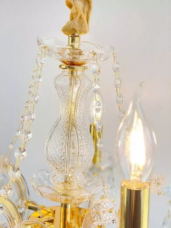 Close-up of gold crystal chandelier with ornate glass design and LED light, featuring hanging cut lead crystal accents.